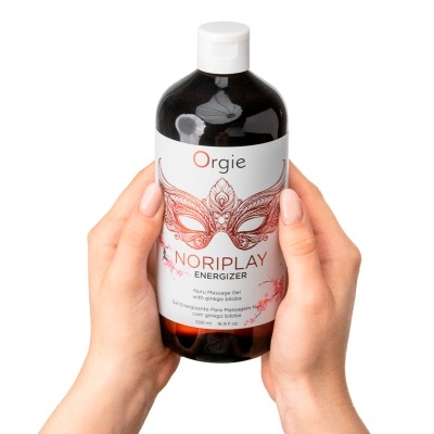 Frasco escuro de gel para massagem com rótulo branco e detalhes vermelhos, segurado por mãos com unhas cor de pele.