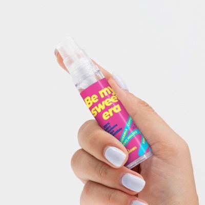 Frasco spray com rótulo colorido segurado por mão feminina.