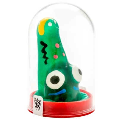 Brinquedo verde abstrato com olhos grandes dentro de invólucro plástico transparente e base vermelha