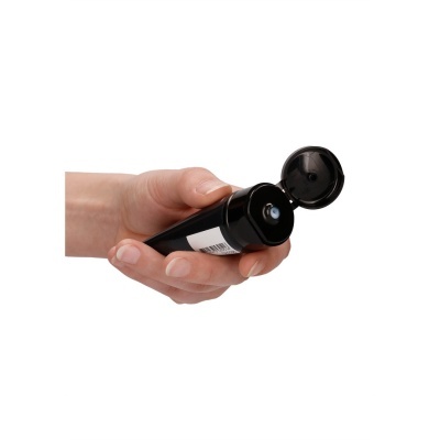 Mão segura tubo preto com tampa aberta e ponto azul na saída do produto