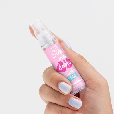 Frasco pequeno de spray com rótulo rosa e texto, segurado por mão com unhas brancas