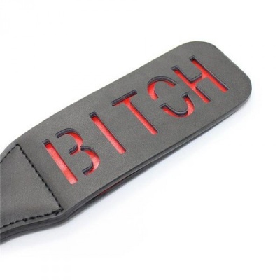 Pala preta de couro com a palavra BITCH recortada e fundo vermelho