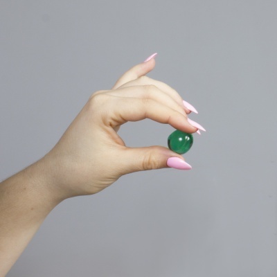 Mão feminina a segurar pedra verde polida com unhas rosas em fundo cinzento