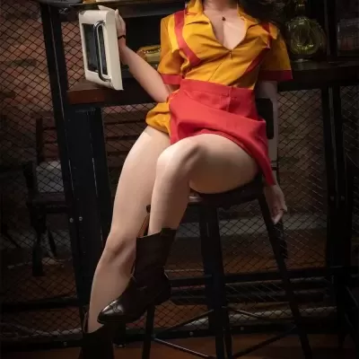 Boneca realista vestindo uniforme amarelo e vermelho, sentada em banco alto segurando bandeja com comida