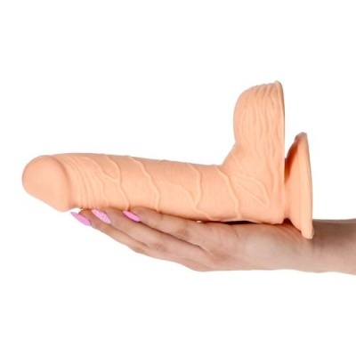 Dildo cor de pele com textura veiculada segurado por mão com unhas cor de rosa