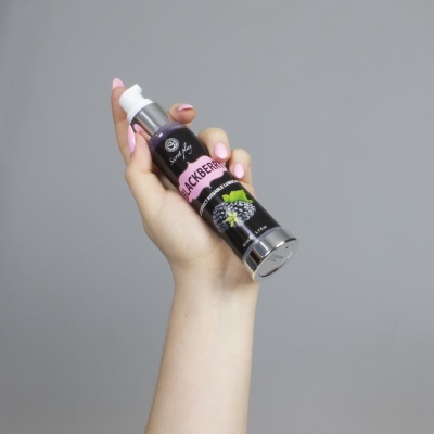 Mão com unhas cor-de-rosa a segurar spray com rótulo de amoras preto e rosa