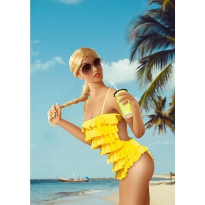 Boneca com fato de banho amarelo, óculos de sol e copo na praia