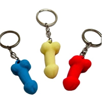 Porta-chaves em forma de osso de cores azul, amarelo e vermelho com argolas metálicas.