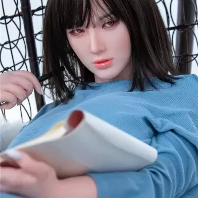 Boneca realista sentada numa cadeira de vime segurando um livro