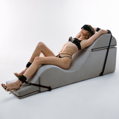 Mulher de lingerie preta reclinada em chaise longue cinza com tiras de fixação em fundo branco