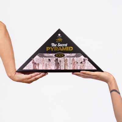 Caixa triangular preta com texto e ilustrações egípcias, segura por duas mãos.