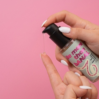 Frasco com doseador preto a libertar líquido transparente para o dedo numa mão, fundo rosa.