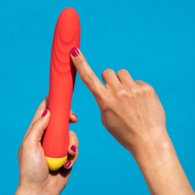 Vibrador vermelho com base amarela e mãos femininas segurando e tocando-o