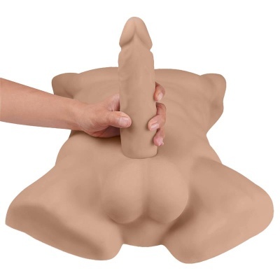 Torso masculino em material macio bege com genitais protuberantes sendo segurados por uma mão