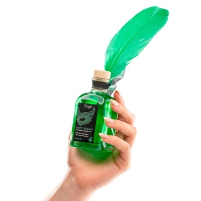 Frasco verde com pena verde e rótulo preto segurado por mão feminina.