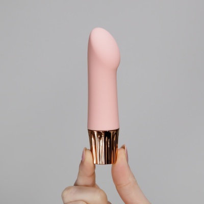 Vibrador cor-de-rosa com base metálica dourada em fundo cinzento.