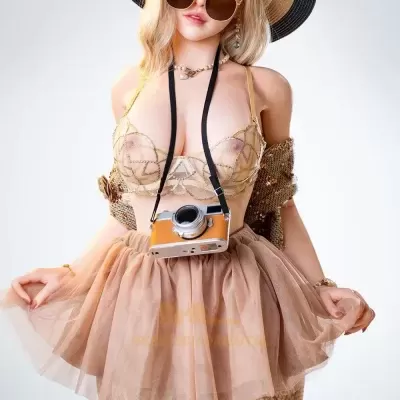 Boneca realista com chapéu, óculos, sutiã transparente, saia de tule bege, meias rendadas e câmara fotográfica