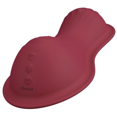Dispositivo vermelho em silicone com botões e formato anatómico sobre fundo branco.