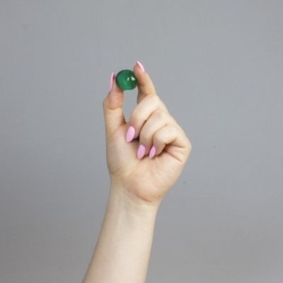 Mão com unhas pintadas de rosa segurando uma esfera verde