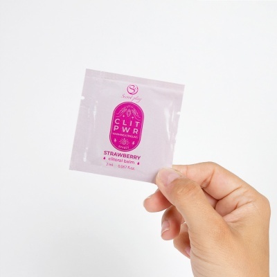 Pacote rosa claro de bálsamo clitoral de morango com texto roxo segurado por mão