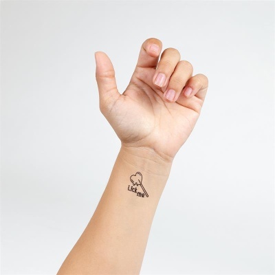 Braço com tatuagem temporária de pirulito em forma de coração e texto Lick me no pulso