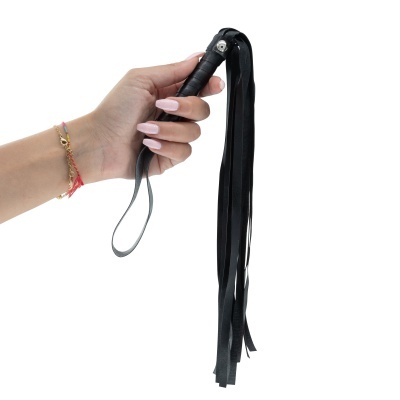 Mão segurando chicote preto de couro com tiras.