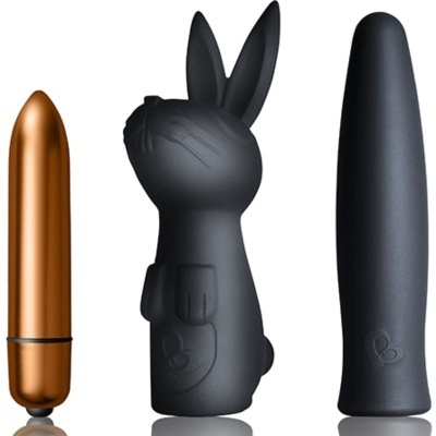 Três dispositivos masculinos em plástico preto e cobre, incluindo um coelho e dois vibradores cilíndricos.