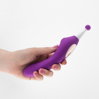 Dispositivo roxo com ponta branca e bola, segurado por mão com unhas rosas.
