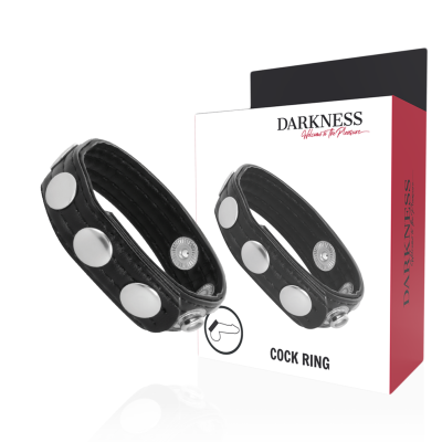 Anel para pénis preto com botões metálicos ao lado de embalagem branca e vermelha da marca DARKNESS