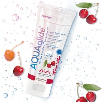 Tubo branco de lubrificante médico Aquaglide sabor cereja com cerejas vermelhas ao fundo