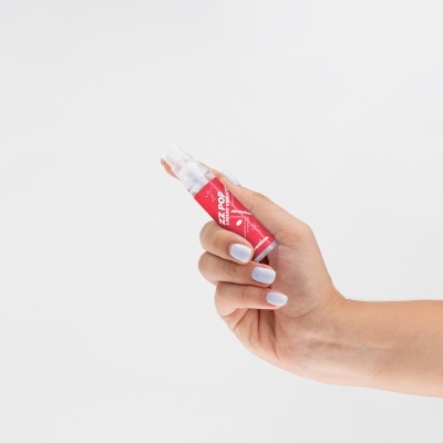 Mão segura frasco pequeno de spray com rótulo vermelho e texto branco