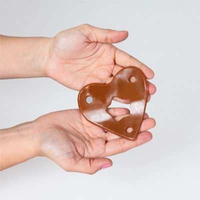 Peça em forma de coração castanha com furos e recorte nas mãos sobre fundo branco