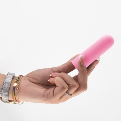 Mão a segurar objeto cilíndrico rosa com fundo branco