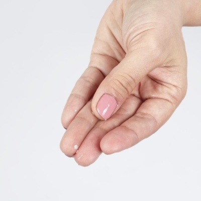 Mão feminina com unhas pintadas de rosa claro e gotas de água