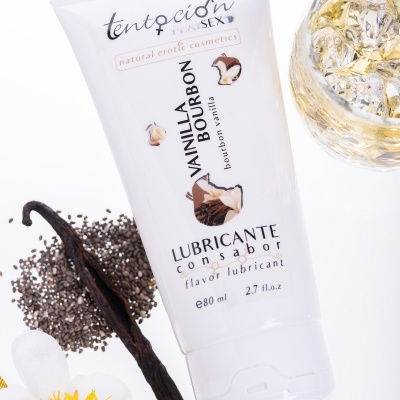 Tubo branco de lubrificante com sabor Vainilla Bourbon junto de vagem de baunilha, sementes e copo de vidro com gelo