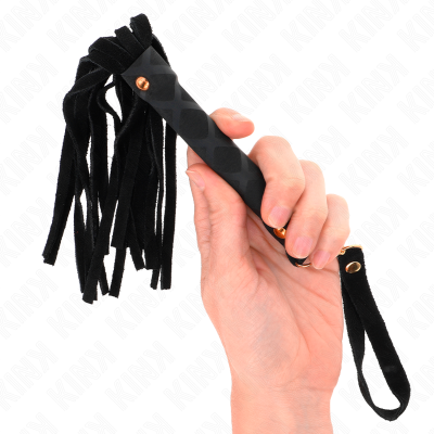 Chicote negro com tiras de tecido e cabo com detalhes metálicos, segurado por uma mão.