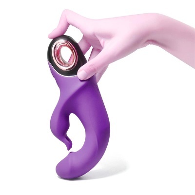 Vibrador roxo anatómico em silicone segurado por mão ao fundo branco
