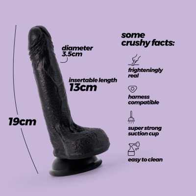 Dildo preto com ventosa na base e descrições de características em texto preto sobre fundo lilás
