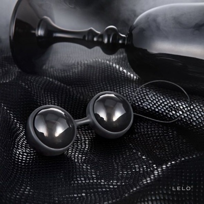 Bolas esféricas pretas brilhantes e cabo preto sobre tecido texturizado preto com copo e texto LELO®