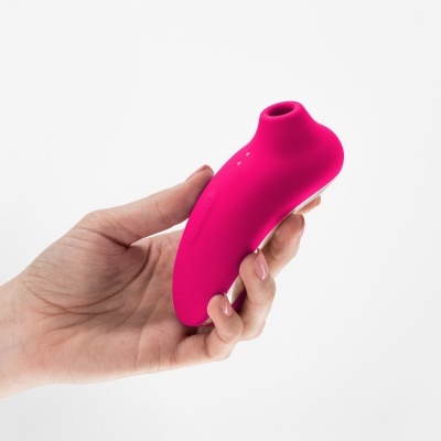 Dispositivo rosa em material silicone, segurado numa mão, fundo branco