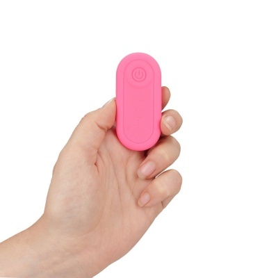 Comando remoto rosa pequeno com botão power numa mão, fundo branco.