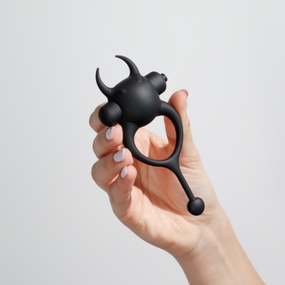 Anel preto em silicone com chifres e haste, segurado por uma mão.