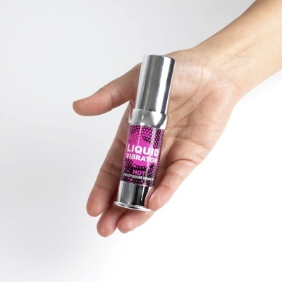 Frasco prateado com rótulo roxo LIQUID VIBRATOR na mão