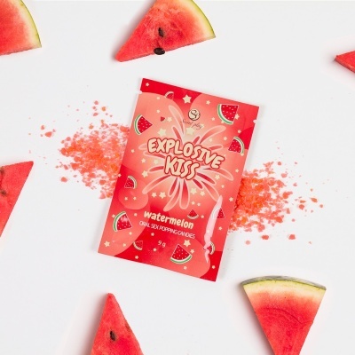 Pacote vermelho de candies explosivos com sabor a melancia junto a pedaços de melancia fresca e cristais vermelhos.
