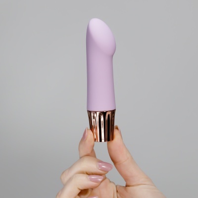 Produto rosa claro com base metálica dourada segurado por uma mão com unhas pintadas de rosa claro