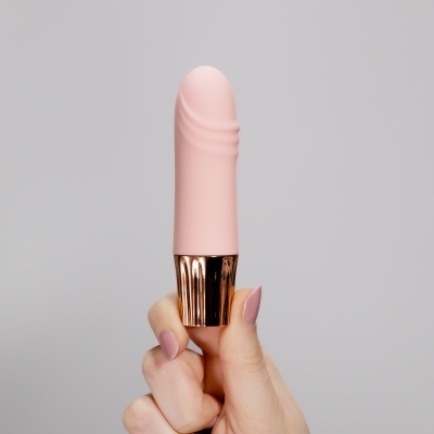 Dispositivo rosa com base dourada segurado por mão com unhas pintadas cor rosa