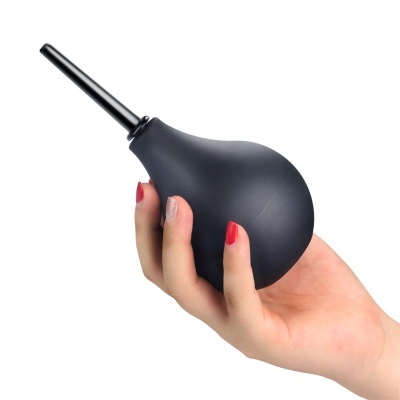Conta-gotas preto com bico longo segurado por mão com unhas vermelhas e bege.