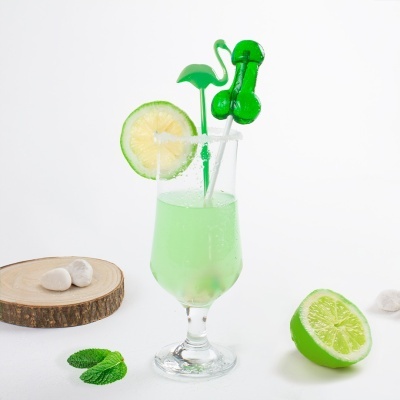 Bebida verde em copo decorado com rodela de lima e acessórios verdes, folhas de hortelã e meia lima junto com pedras sobre disco de madeira.