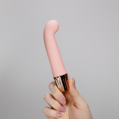 Mão com unhas rosas a segurar objeto cor de rosa claro com base dourada.