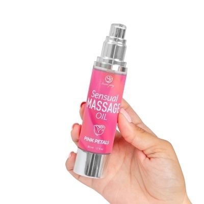 Frasco rosa de óleo de massagem sensual com tampa metálica prateada, na mão.
